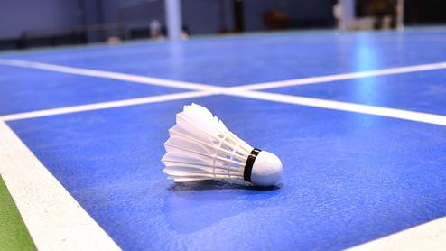 Nahaufnahme eines Federballs auf einem blauen Badmintonfeld mit weißen Linien.