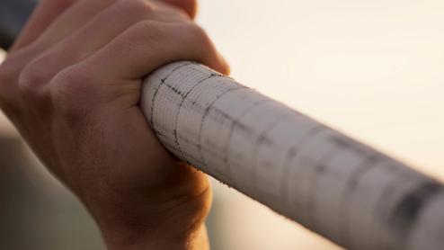 Nahaufnahme einer Hand, die einen mit Band umwickelten Hantelstange fest umgreift, vor einem unscharfen Hintergrund.