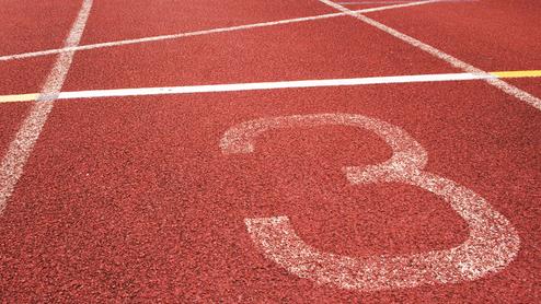 Nahaufnahme eines roten Laufbahnabschnitts mit der Markierung der Bahn 3 und weißen Linien.