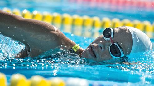 Schwimmerin in einem Wettkampf mit einer weißen Badekappe und Schwimmbrille, die durch das Wasser gleitet.