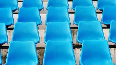 Reihe blauer Kunststoffstühle auf einer Tribüne, gleichmäßig angeordnet mit Sicht auf die Sitzflächen.