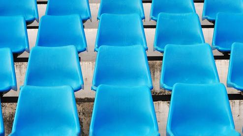 Reihe blauer Kunststoffstühle auf einer Tribüne, gleichmäßig angeordnet mit Sicht auf die Sitzflächen.
